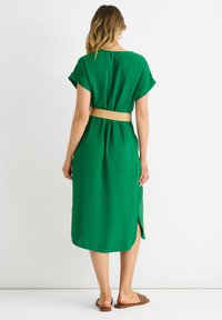 Abito midi verde con maniche corte e vestibilità morbida, dotato di una cintura in vita e fessure laterali. Tessuto liscio e materiale leggero.