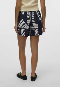 Shorts bleu marine avec un motif géométrique blanc, présentant une coupe décontractée, un tissu texturé et une taille élastique. Des chaussures plates noires complètent la tenue.