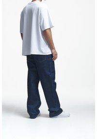 Camiseta blanca de algodón de manga corta, combinada con jeans de mezclilla azul oscuro de corte holgado, que cuentan con dos bolsillos traseros y un diseño de pierna recta.