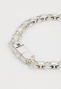 Sudraba ķēdes rokassprādze ar maiņojošiem gludajiem un teksturētajiem taisnstūra saitēm un aizdari, uz kuras ir iegravēts "MAPLE" un kroņa logo.