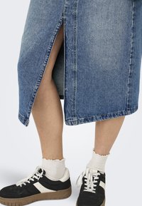 Denim krilo s stranskim razporkom, modre barve, raztrgani rob, oblečeno z črnimi supergami in belimi čipkastimi nogavicami.