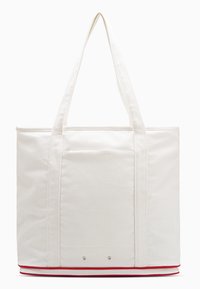 Bijela platnena torba s crvenim donjim rubom, dvostrukim ručkama za nošenje i prednjim džepom. Glatka tekstura s definiranim pravokutnim oblikom.