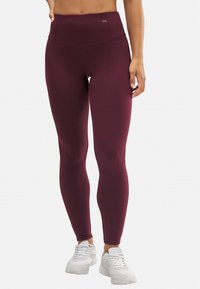 Mallas de tiro alto burdeos hechas de tela elástica. Presentan una textura suave y una mínima marca en la cinturilla.