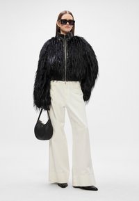 Jaqueta cropped em pelo sintético preto com colarinho de couro, combinada com calças brancas de cintura alta e perna larga, e uma pequena bolsa preta.