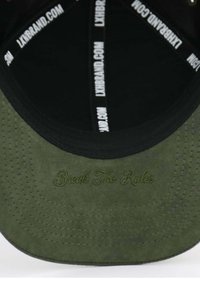 Grüner Wildlederhut mit schwarzem Schirm. Das Innere hat ein schwarzes Futter mit weißem Text und "Break The Rules" in Grün gestickt.