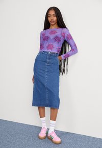 Haut à manches longues violet avec un motif floral, associé à une jupe en denim bleu taille haute et des baskets roses avec des rayures vertes.
