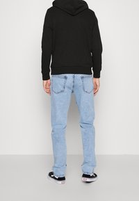 Svart hoodie med känguruficka, blå denimjeans och svarta sneakers. Syntetisk sömnad och klassisk femficksdesign på jeansen.