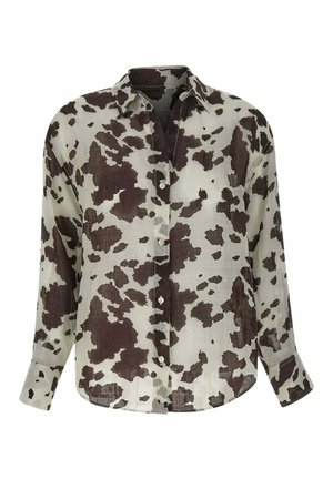 Chemise à manches longues avec boutons, motif vache noir et blanc, col classique et coupe décontractée, présentée sur fond blanc.