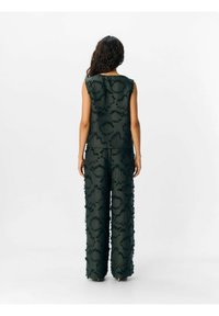Haut sans manches vert foncé et pantalon large avec un motif floral texturé, présentant des accents frangés et une coupe décontractée.