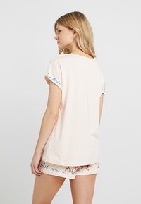 Light pink t-shirt with short sleeves, featuring floral-patterned cuffs. Soft fabric, loose fit, and a rounded neckline, paired with patterned shorts.