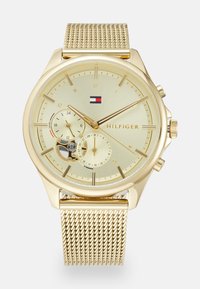Montre dorée avec un cadran rond, un bracelet en maille, des marqueurs d'heure minimalistes, un sous-cadran pour la date et un logo. Cadran doré clair avec une finition brossée.