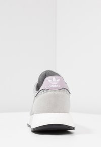Sneaker in suede grigio e mesh visto da dietro, con un inserto per il tallone in lavanda con logo Adidas e intersuola bianca, texture con un motivo a punti.