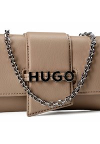 Clutch color beige chiaro in materiale testurizzato, con logo "HUGO" nero e tracolla a catena argento. Design elegante e rettangolare con dettagli cuciti.