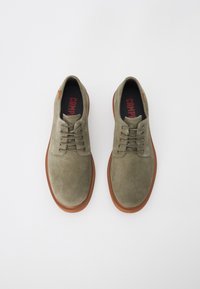 Pantofi din suede verde măsliniu cu sole de cauciuc maro, bot rotund și cinci guri pentru șireturi. Tălpica interioară are inscripția "CAMP" cu litere roșii.