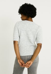 Suéter de punto de manga corta en gris claro con un acabado texturizado, cuello redondo y dobladillo acanalado, combinado con pantalones grises de talle alto.