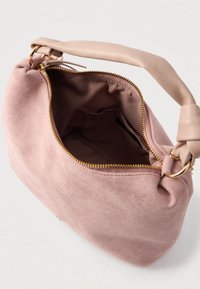 Petit sac à main en daim rose poussiéreux avec une poignée rembourrée douce, fermeture éclair dorée partiellement ouverte dévoilant une doublure intérieure en tissu marron et une poche intérieure.