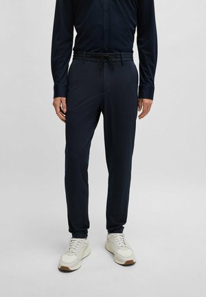 Pantalons fuselés bleu marine avec un motif texturé, taille élastique et cordon de serrage. Associés à des chaussures blanches pour un look décontracté.