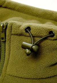 Tissu polaire vert olive avec une fermeture éclair et un verrou de cordon réglable passant à travers des œillets métalliques.