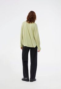 Ανοιχτό πράσινο φαρδύ πουκάμισο με μακριά μανίκια, χαλαρή εφαρμογή, υφή υφάσματος, συνδυασμένο με φαρδιά μαύρα τζιν και χοντρές μαύρες παπούτσια.