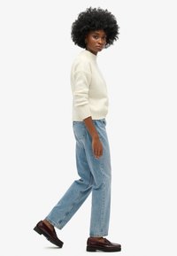 Suéter de crema claro con dobladillo acanalado, ajuste relajado, combinado con jeans rectos de mezclilla azul claro y mocasines burdeos oscuros. Sin patrones visibles.