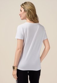 Tricou alb cu mânecă scurtă și decolteu rotund. Fabricat dintr-un material moale, are o croială lejeră și o textură netedă. Este accentuat cu o brățară metalică.