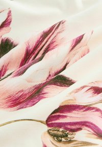 Közeli felvétel krémszínű anyagról, melyen rózsaszín és lila virágminták hajtogatva láthatók, részletes szirmokkal és barna virágközponttal.