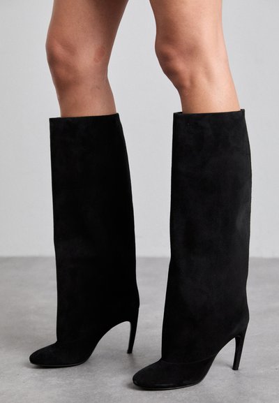 Bottes noires à hauteur de genou en suede doux, avec un bout pointu et un fin talon stiletto. Texture lisse et design sans couture.