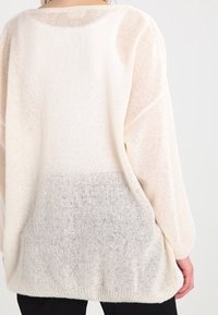 Pull léger couleur crème avec un dégradé vers le gris clair à l'ourlet. Comprend des manches longues, un large décolleté et une finition texturée.