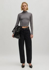Grauer gerippter Rollkragen-Crop-Top, schwarze hochgeschnittene Hose, schwarze übergroße Tasche und spitze schwarze Absatzschuhe mit Schnallen-Detail.