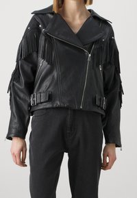 Zwarte leren korte bikerjas met franjes, zilverkleurige ritsen, grote revers en verstelbare riemen met gesp in de taille.