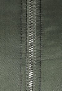 Section en tissu zippée de couleur vert foncé, dotée d'une fermeture éclair métallique, d'une texture textile lisse et de coutures visibles le long du bord.