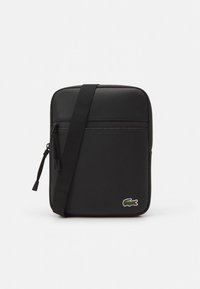 Zwarte schoudertas van gestructureerd synthetisch materiaal. Voorzien van een ritssluiting, verstelbare riem en een klein logo-accent aan de voorkant.