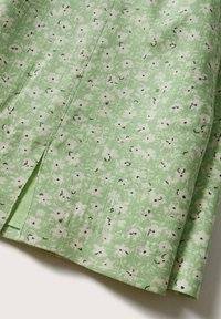 Jupe vert clair avec un motif floral blanc et des accents noir. Elle présente une fente sur le côté et un tissu texturé.