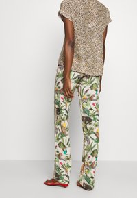 Bluzka w wzory na beżowym tle z czarnymi kropkami, w zestawie z luźnymi spodniami z żywymi wzorami tropikalnej fauny i flory.