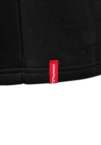 Schwarzes Baumwoll-T-Shirt für den Sport mit abgerundetem Saum und einem roten gewebten Etikett mit dem Markennamen "hummel" auf der linken Seite.