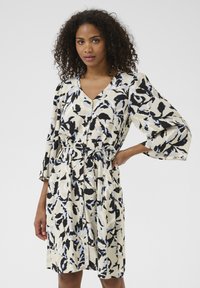 Abito con motivo floreale in crema, nero e azzurro chiaro. Presenta scollatura a V, chiusura a bottoni, vita cintrata con cintura e maniche ampie a campana.