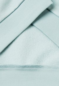 Světle modrý sweatshirt s žebrovanými manžetami, má měkký, strukturovaný vnitřek a hladký povrch s švem na spodním okraji.