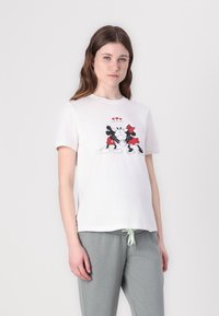 White cotton t-shirt featuring a graphic print of Mickey and Minnie Mouse with red accents and hearts, short sleeves. Paired with gray joggers.