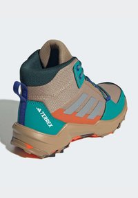 Terrex friluftssko med en beige mesh overdel, blå og teal aksenter, oransje såle og grå striper. Har polstret krage og trekkstang.
