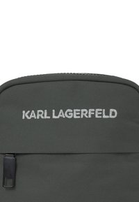 Zaino in nylon grigio con finitura texturizzata, tasca frontale con zip e logo "KARL LAGERFELD" ricamato in lettere bianche.