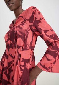 Vestido fluido en un patrón floral en rosa y rojo oscuro. Presenta un escote en V y mangas acampanadas. Hecho de una tela ligera con una cintura ajustada.