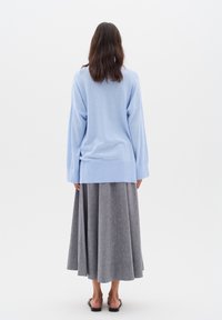 Hellblauer, übergroßer Strickpullover mit langen Ärmeln; kombiniert mit einem fließenden, grauen Plisseerock, der bis zur Mitte der Waden reicht.