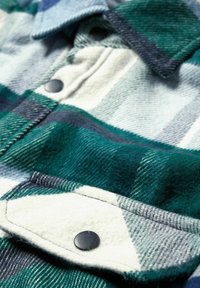 Zielono-niebieska koszula flanelowa w kratę o fakturowanej tkaninie, z czarnymi guzikami i kremową patką na kieszeni. Miękki, przytulny design.