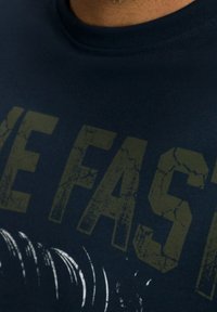 Mjöldblå bomulls t-shirt med spruckna, djärva bokstäver i olivgrön som står "LIVE FAST" med grafisk detalj längst ner.