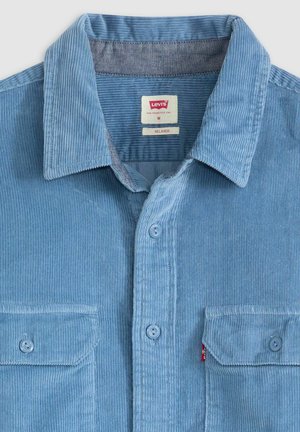 Camicia di velluto a coste blu con una vestibilità rilassata, caratterizzata da un colletto button-down, due tasche sul petto e una texture sottile ottenuta da righe verticali.