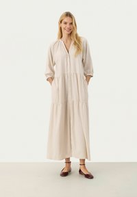 Rochie din in de un bej deschis, cu deschidere pe butoane, talie gathered și mâneci trei sferturi. Prezintă buzunare laterale și un design maxi, fluid.