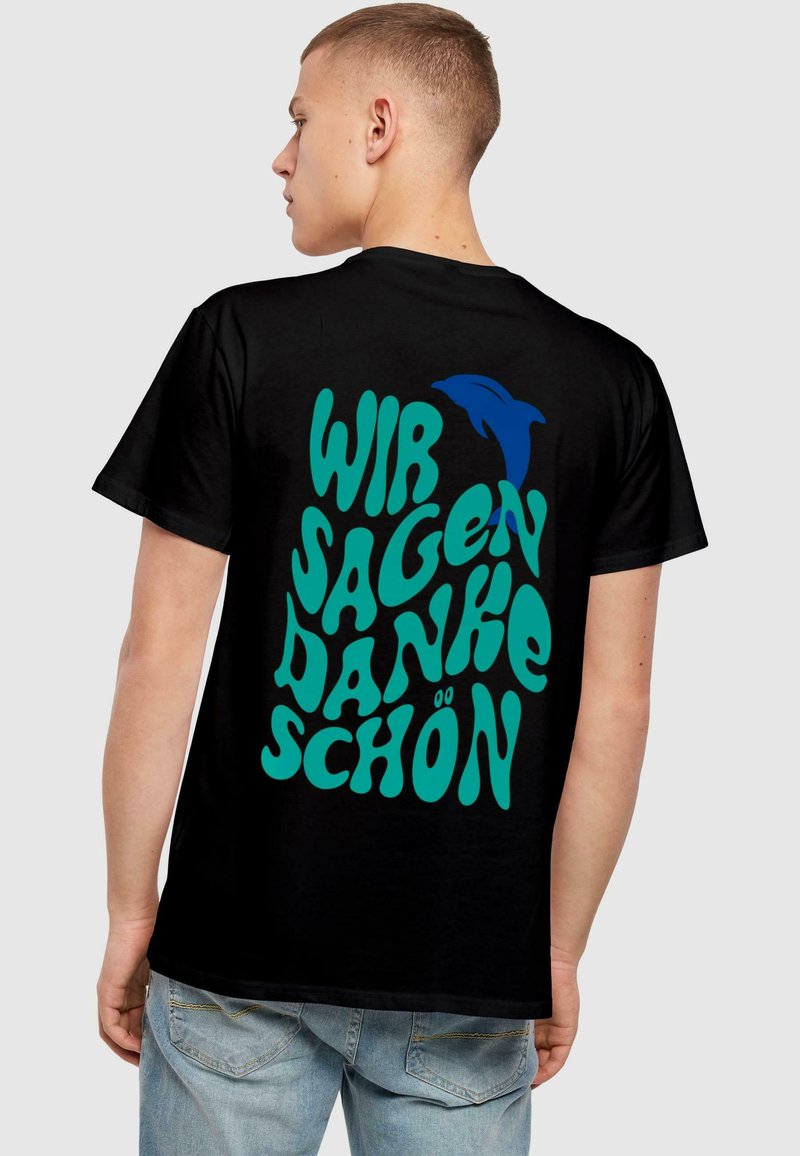 Sort bomulds t-shirt med stor, turkise boble-agtig tekst der siger "WIR SAGEN DANKE SCHÖN" og et lille blåt delfin grafik.