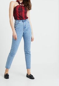Czerwony top halter w wężowy wzór z okrągłym detalem, w połączeniu z jasnoniebieskimi spodniami typu high-waisted i czarnymi loaferami. Gładkie faktury w całej stylizacji.