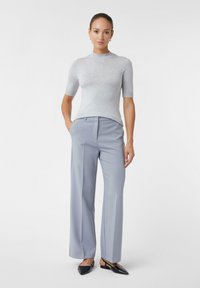 Szary prążkowany top z krótkim rękawem w połączeniu z jasnoszarymi szerokimi spodniami o eleganckim kroju. Modelka nosi czarne płaskie buty. Gładkie białe tło.