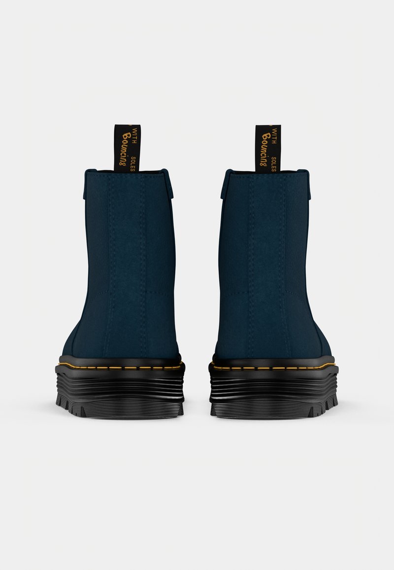Bottines bleu marine avec une tige en tissu texturé, semelle en caoutchouc noir et détails de couture jaunes, comprenant un tirant au niveau du talon.